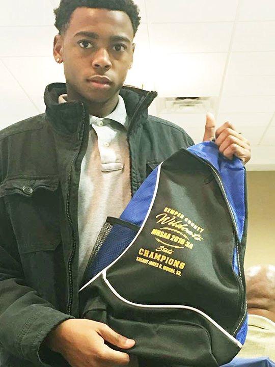 Young man in a black jacket holding Kemper County Wildcats backpack